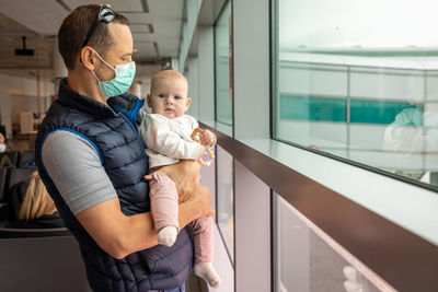 Father holding daughter standing by widow at airport