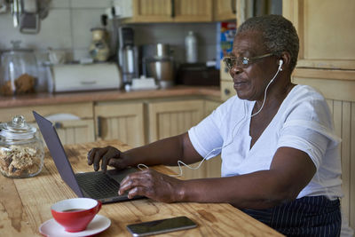 Senior woman sitting at kitchen table using laptop