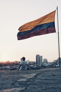 Rear view of man flag on city against sky during sunset