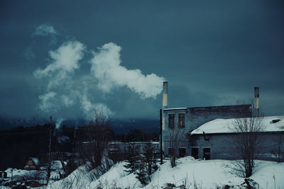 Snow covered factory against sky during winter