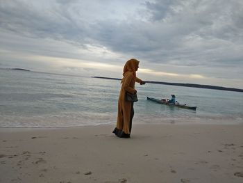 Woman standing on beach against sky during sunset