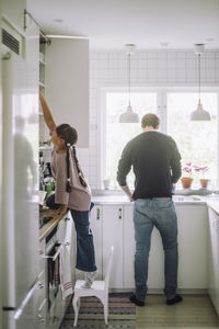 Girl reaching at cabinet with father preparing food in kitchen at home