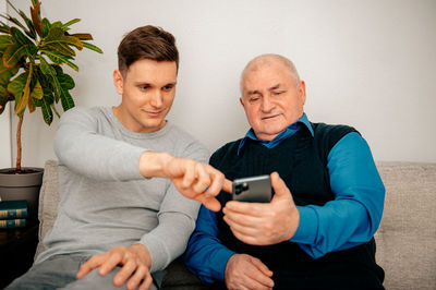 Father and son using phone sitting on sofa