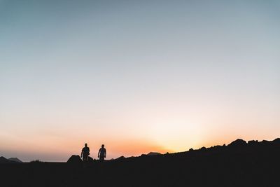 Silhouette people on landscape against sky during sunset