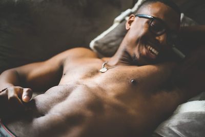 Shirtless smiling young man lying on bed at home