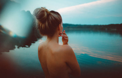Rear view of naked woman standing against lake