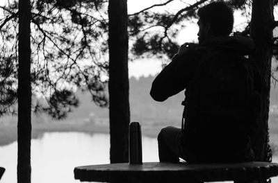 Rear view of silhouette man sitting by tree trunk