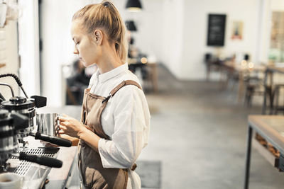 Young female barista using espresso maker at cafe