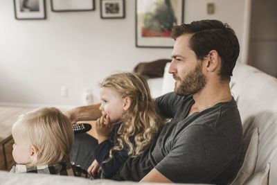 Mid adult father with daughters watching tv in living room at home