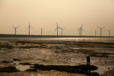 Wind turbines on silhouette landscape against sky
