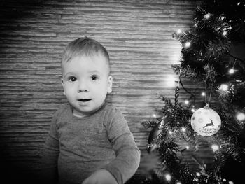 Portrait of boy by illuminated christmas tree against wall