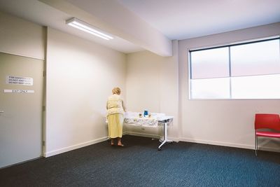 Full length rear view of woman standing by table in room