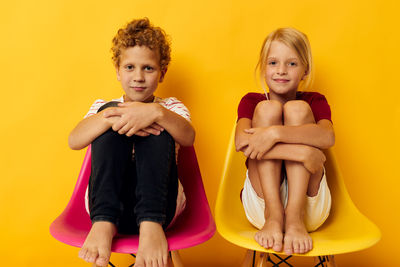 Full length of sibling sitting against yellow background