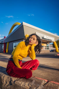 Young woman sitting against yellow wall