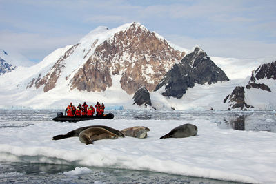 People in inflatable raft on sea by snowcapped mountain during winter