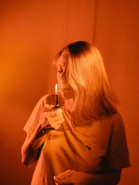 Young woman standing against orange wall