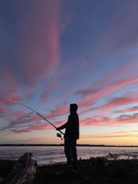 Silhouette man fishing by sea against sky during sunset