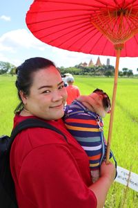 Portrait of mid adult woman with pug carrying red umbrella standing on landscape