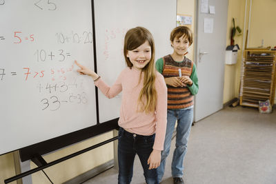 Happy girl solving maths problem with boy in classroom