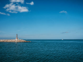 Lighthouse by sea against blue sky