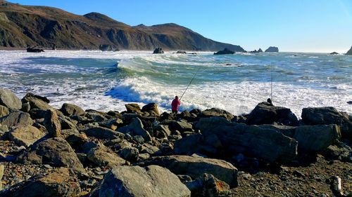 Person fishing at beach against mountains