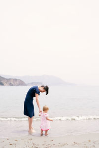 Rear view of mother and daughter on beach against sky