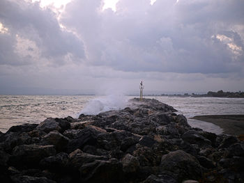 Lighthouse on rocks by sea against sky