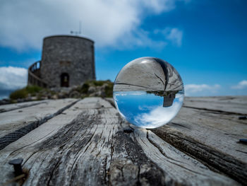 Close-up of crystal ball on wood against sky