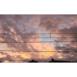 Low angle view of electricity pylon against cloudy sky