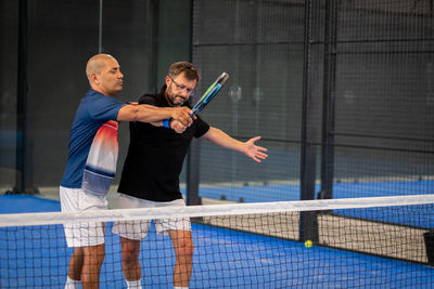 Monitor teaching padel class to man, his student - trainer teaches boy how to play padel on indoor 