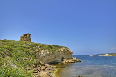 Rock formations by sea against clear blue sky