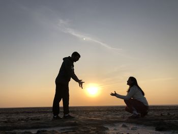 Couple gesturing at beach during sunset