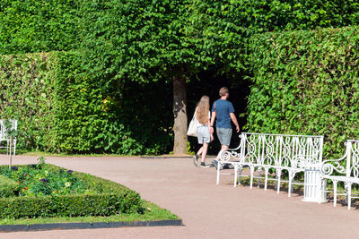 A young guy in a blue t-shirt and a blonde with long hair are walking through a green park.