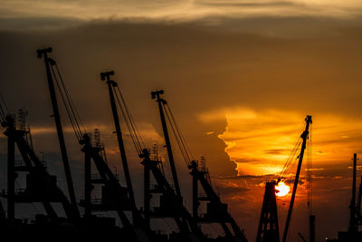 Silhouette cranes at commercial dock against sky during sunset