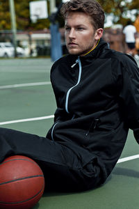 Man looking away while sitting on ball on field