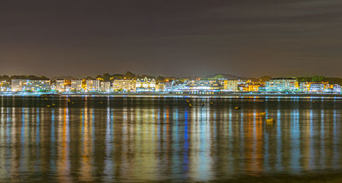 Illuminated buildings by sea against sky at night