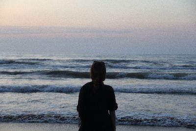 Rear view of woman standing at beach during sunset