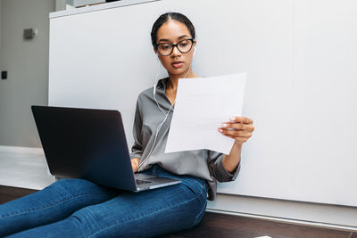 Woman reading paper while working on laptop at home