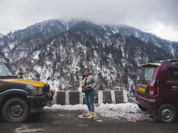 Man standing by car on mountain road during winter