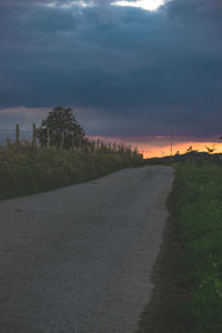 Road by trees against sky during sunset