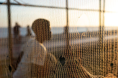 Silhouette of people, through a safety net, walking along the edge of a beach in the late afternoon