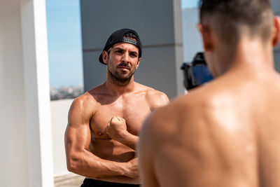 Shirtless man photographing macho friend