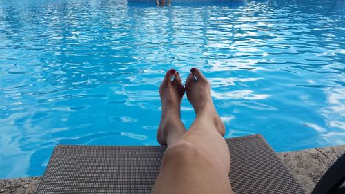 Low section of woman relaxing on deck chair at poolside