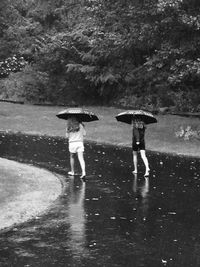 Rear view of woman standing on wet road during rainy season
