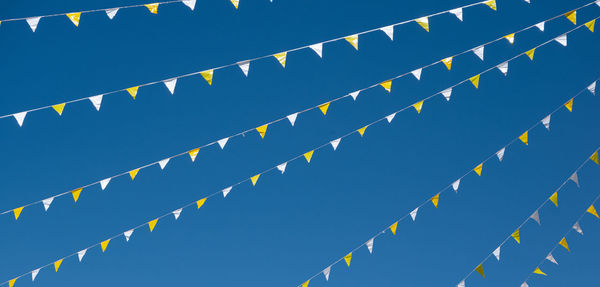 Low angle view of flags hanging against clear blue sky