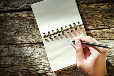 Cropped hand holding pencil over note pad on table