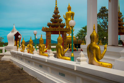 Golden statues of buddha are lined up in the temple wall.