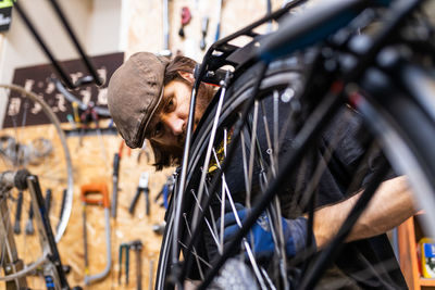 Mature bearded mechanic in workwear and gloves checking and repairing wheel of bike during maintenance service in workshop