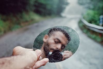 Reflection of man photographing with camera on wet mirror over road