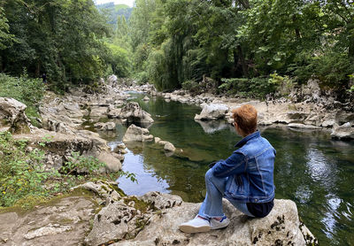 Man sitting on rock by river in forest